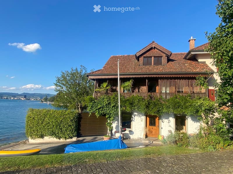 Two-story house with a tiled roof, balcony, garage, and scenic lake view.