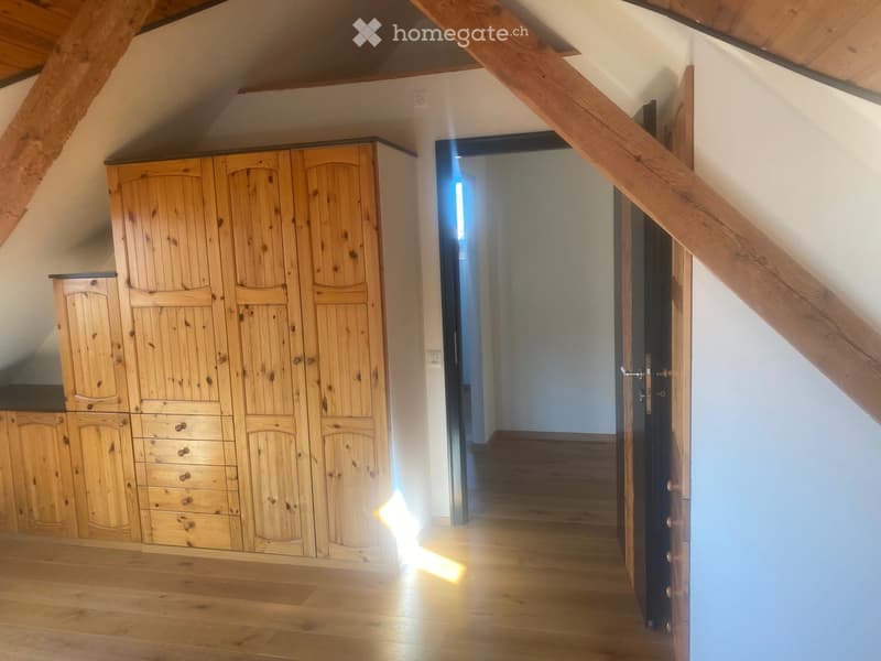 A wooden-floored hallway with a large wooden wardrobe on one side and a staircase leading upwards, featuring exposed wooden beams on the ceiling.