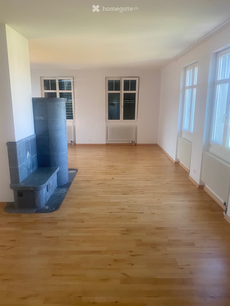Empty room with wooden flooring, white walls, and multiple windows. A built-in fireplace is visible on the left side.