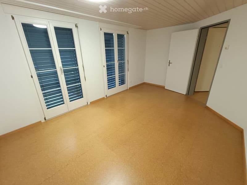 Empty room with light wooden flooring, white walls, and large windows with shutters. No furniture or equipment present.