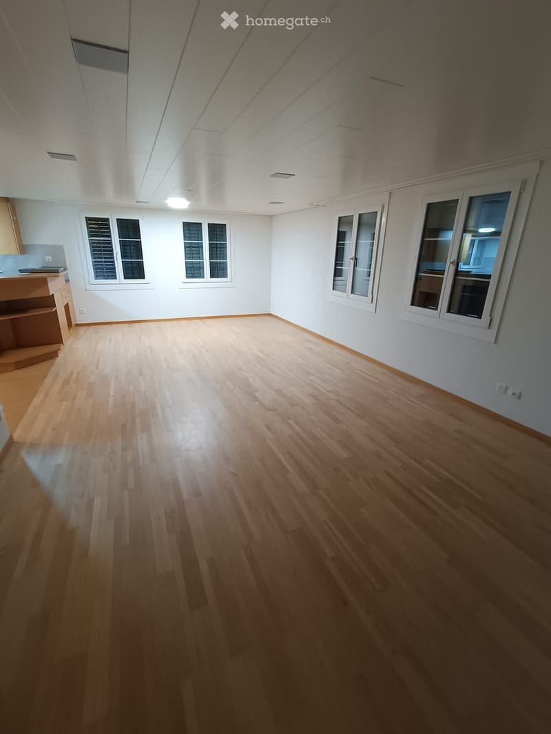 empty room with hardwood floors, white walls, white ceiling, three windows, and a small cabinet on the left