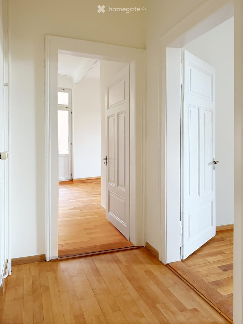 Empty hallway with light wooden flooring, white walls, and several closed doors leading to other rooms.