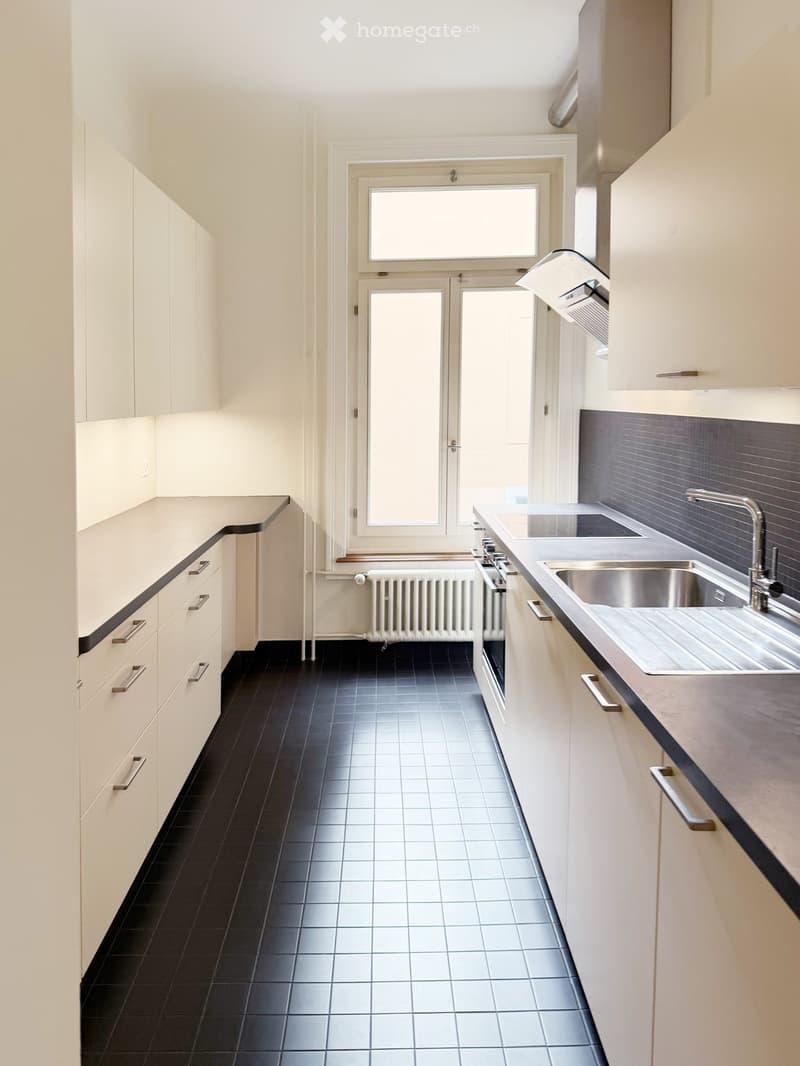 Modern kitchen with white cabinets, black tiled floor, stainless steel sink, and a windowed door leading outside.