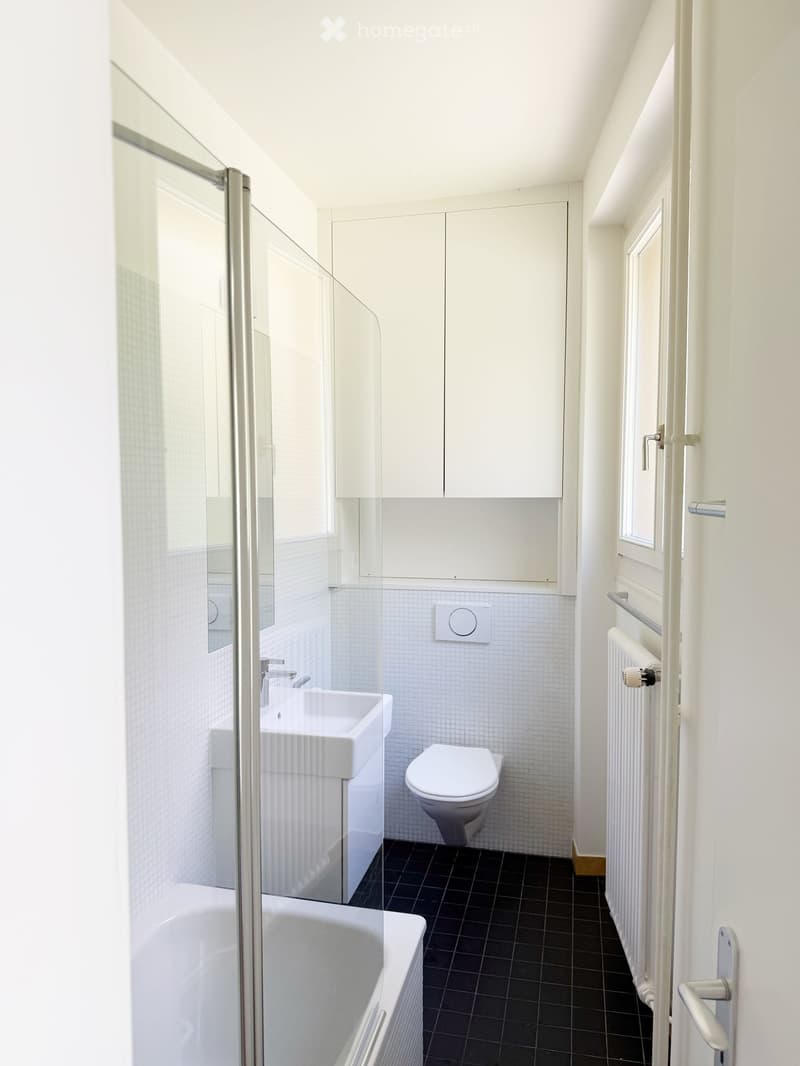 Modern bathroom with white tiles, black floor, sink, toilet, bathtub, radiator, and built-in cabinets.