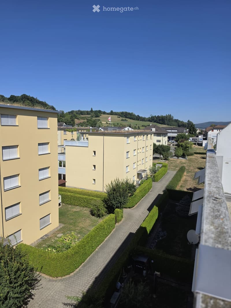 Multi-story residential building with yellow facade, multiple windows, balconies, and surrounding greenery.