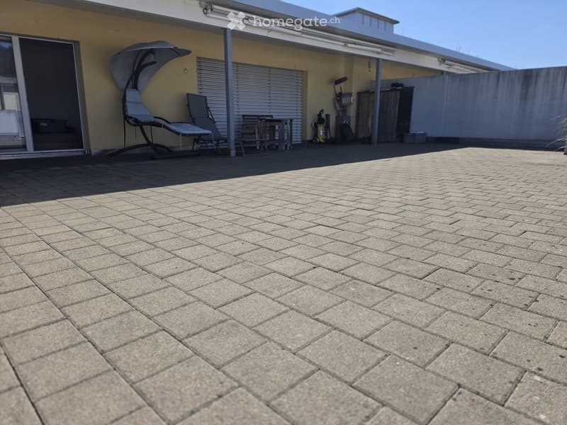 Brick-paved outdoor area with a sun lounger, table, chairs, and storage cabinet near a covered patio.