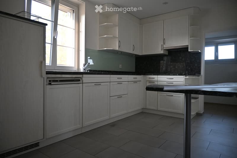 Modern kitchen with white cabinets, black countertops, tiled floor, and a built-in dishwasher. Features a central island with a black countertop and a faucet above the sink.