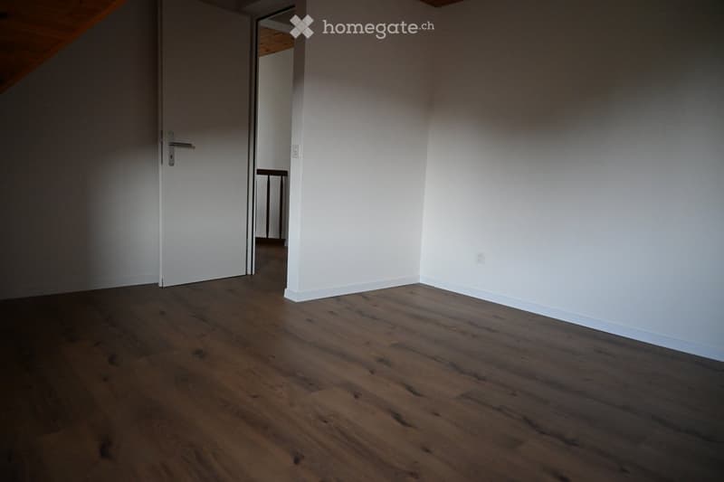 Empty room with wooden flooring and white walls, featuring a closed door and visible baseboard trim.