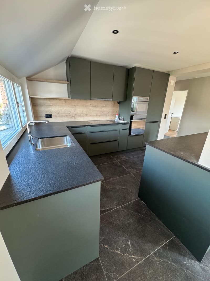 Modern kitchen with dark grey cabinets, black countertops, stainless steel sink, and built-in appliances.