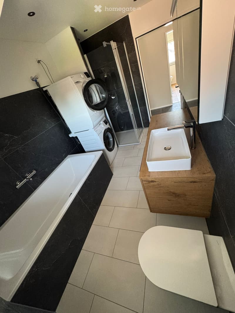 Modern bathroom with black marble floors, white bathtub, sink, toilet, and a washing machine/dryer unit in the corner.