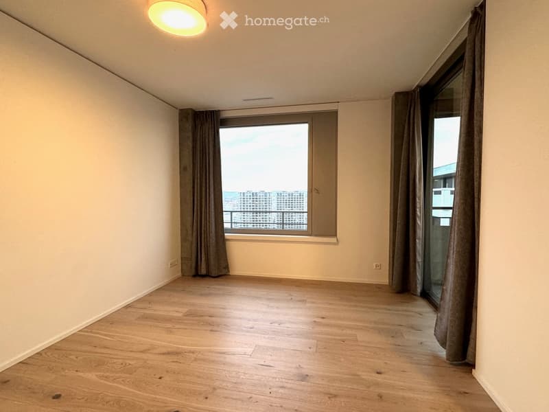 Empty room with wooden flooring, large windows with curtains, and a view of the cityscape.