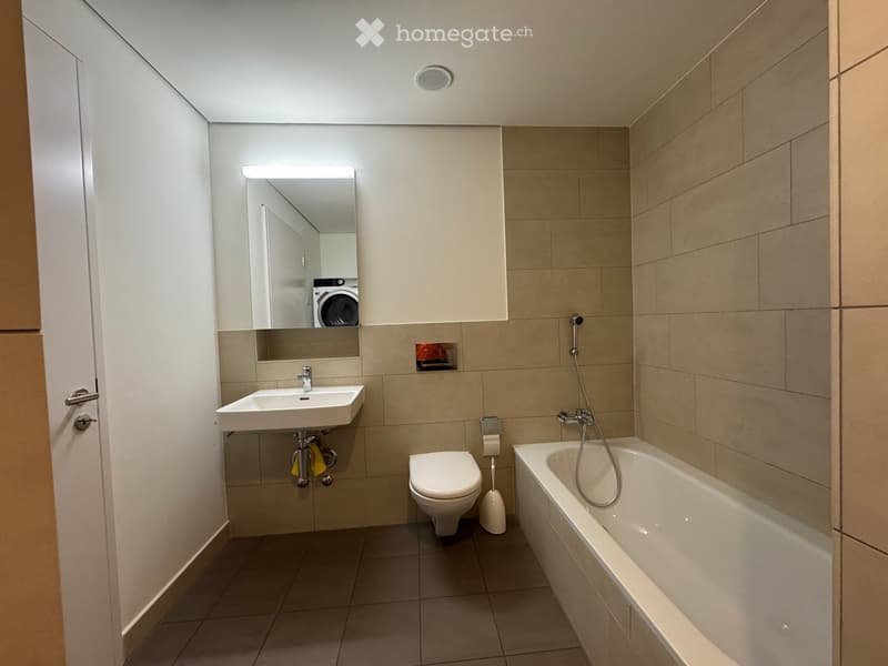 Modern bathroom with a sink, toilet, bathtub, and mirror. Beige tiles and a sleek design.