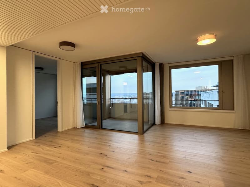 Empty room with wooden flooring, large windows, and sliding glass doors leading to a balcony.