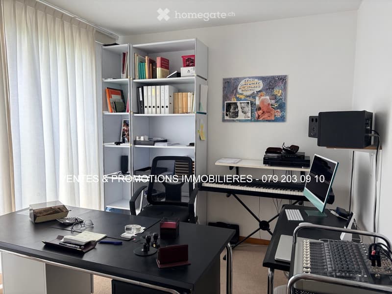 A well-organized office space with a large desk, ergonomic chair, laptop, keyboard, and a shelf filled with books and binders. A piano and speaker system are also present, along with a framed picture on the wall.
