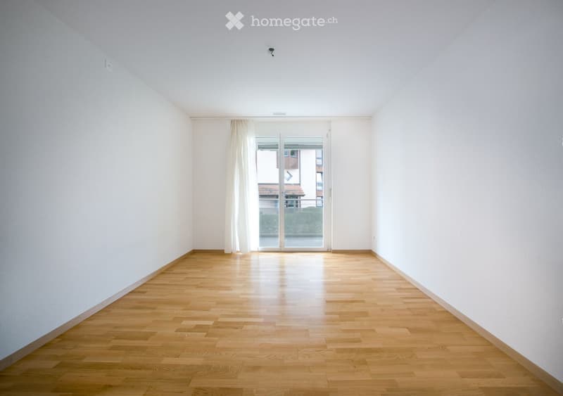 Empty room with light wooden flooring and white walls, featuring a large glass door leading to a balcony or outdoor area.