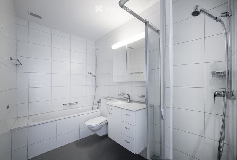 Modern bathroom with white tiles, a bathtub, toilet, sink, mirror, and a glass-enclosed shower area.