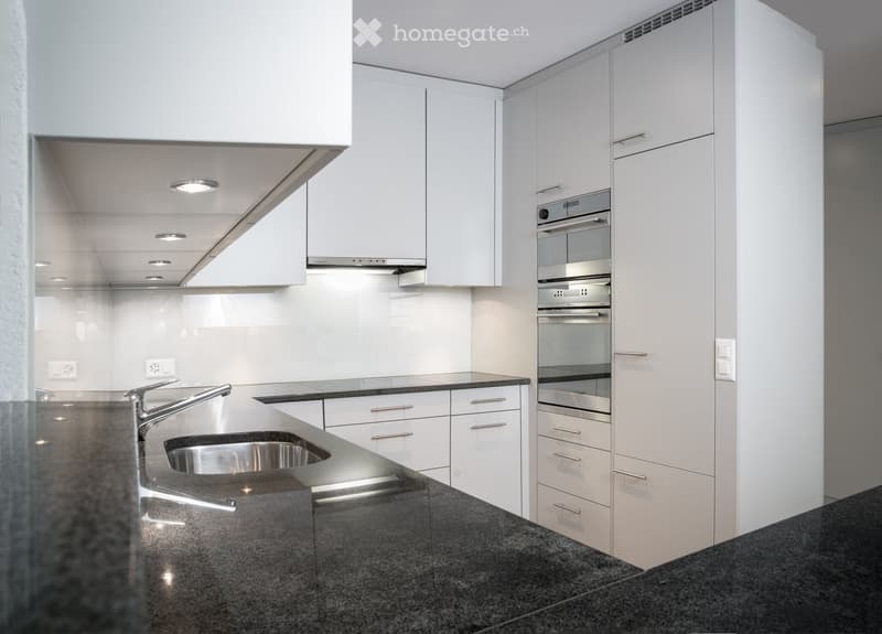 Modern kitchen with white cabinets, stainless steel sink, and built-in oven. Features granite countertops and dark flooring.