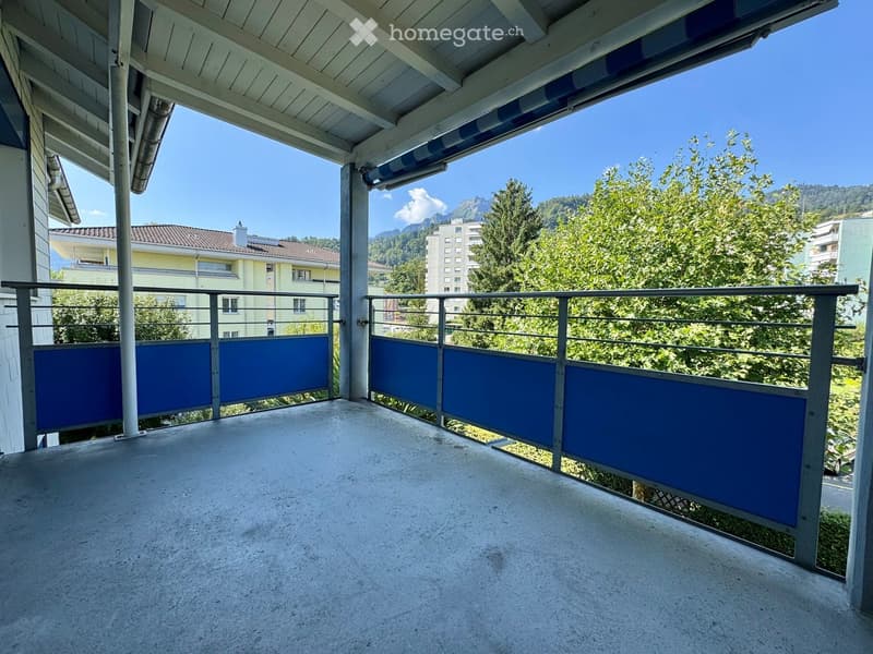 Balcony with metal railings, blue privacy screens, and a view of trees and buildings.