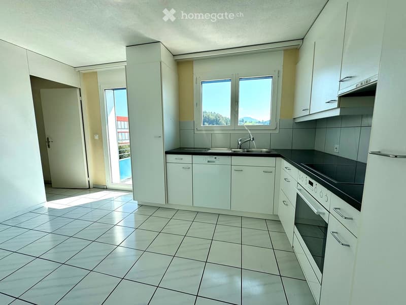 Modern kitchen with white cabinets, tiled floor, sink, oven, dishwasher, and large windows offering a view.