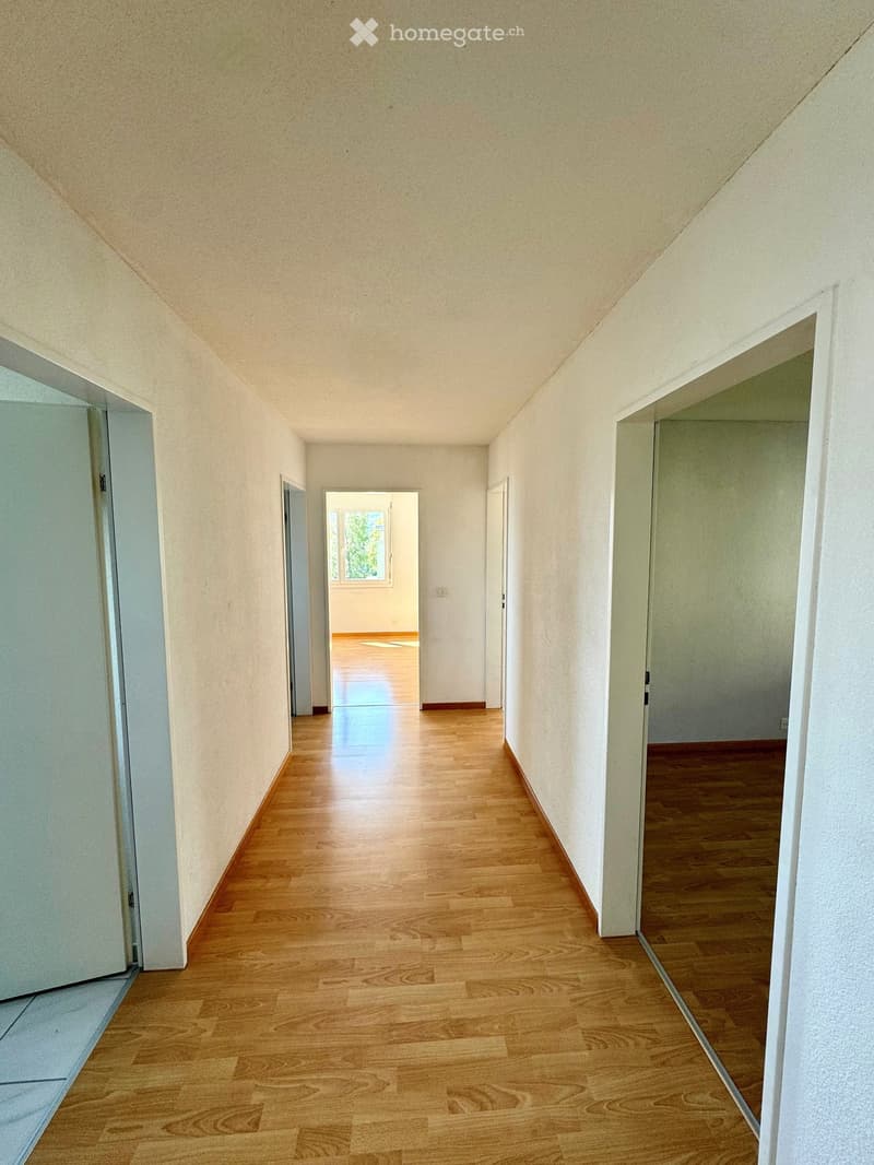 Empty hallway with wooden flooring, white walls, and several doors leading to other rooms.