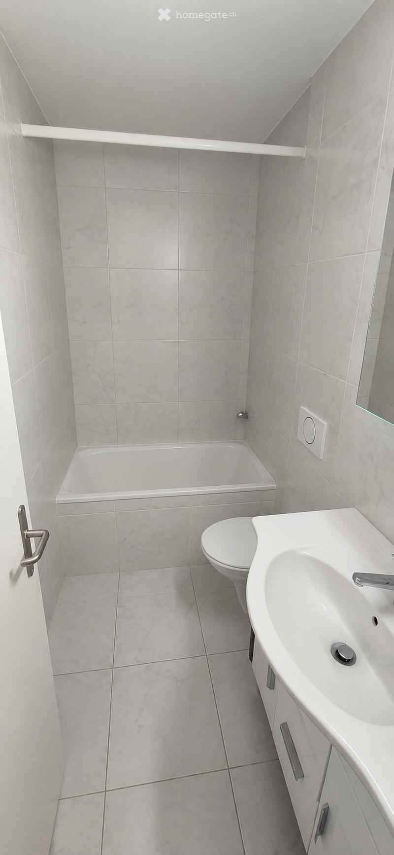 Modern bathroom with marble tiles, a bathtub, toilet, sink, and cabinet.