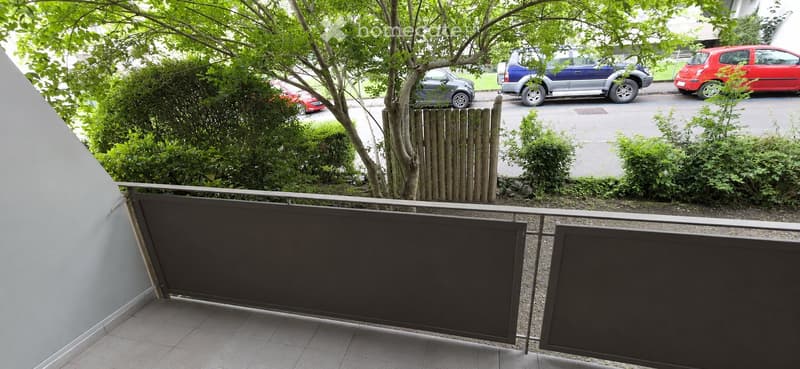 Balcony with metal railing, tiled floor, and view of a street with parked cars and greenery.