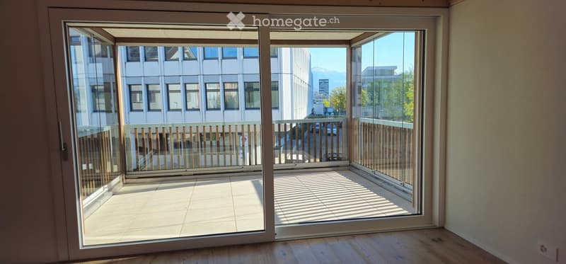 Empty room with wooden flooring, large sliding glass doors leading to a balcony with wooden railings and tiled flooring.