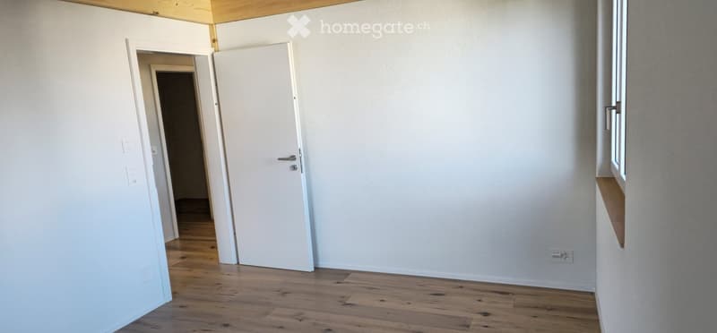 Empty room with white walls, wooden flooring, and a white door leading to another room.