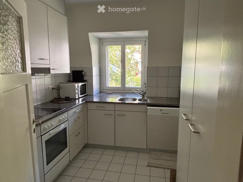 Modern kitchen with white cabinets, stainless steel appliances, tiled floor, and a window overlooking greenery.