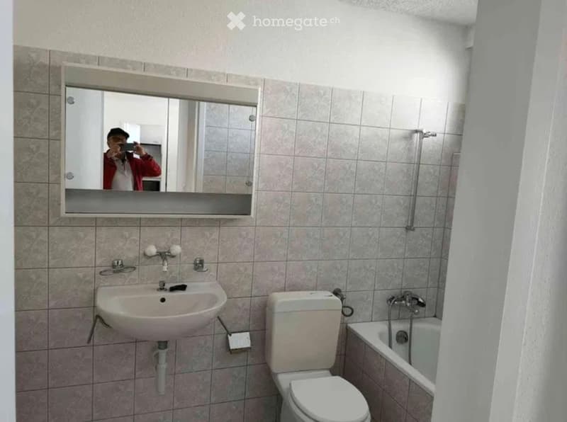 Bathroom with tiled walls, a white sink, a toilet, a bathtub, and a large mirror above the sink.
