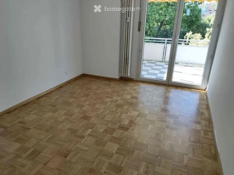 Empty room with wooden herringbone flooring, white walls, and large sliding glass doors leading to a balcony.