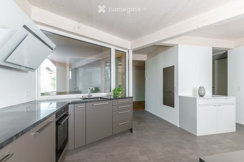 Modern kitchen with grey cabinets, stainless steel appliances, and a large window overlooking the outdoor area.