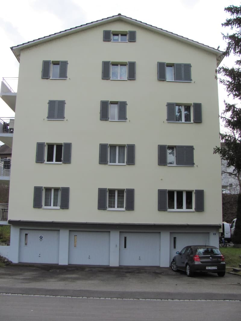 A 4 story apartment building, white walls, gray windows, 3 garages on the bottom floor