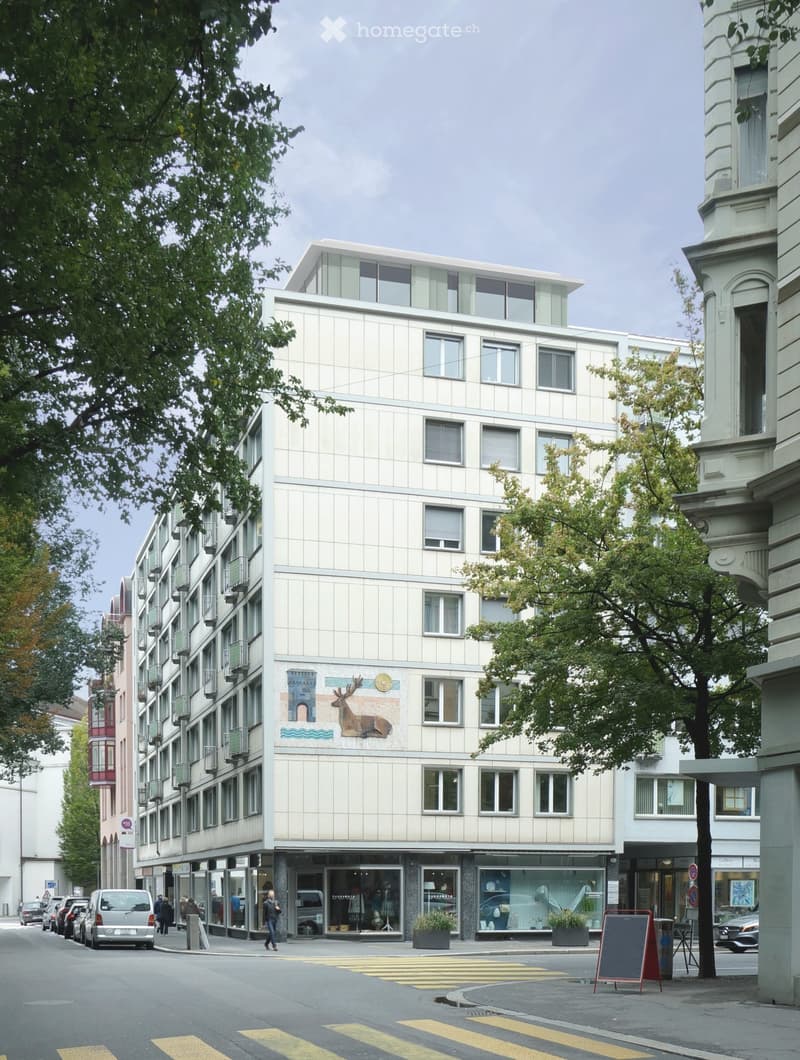 Modern multi-story building with large windows and a decorative mural of a deer on the facade. The ground floor features storefronts with glass displays and potted plants. The building is situated on a street corner with a pedestrian crossing in front.