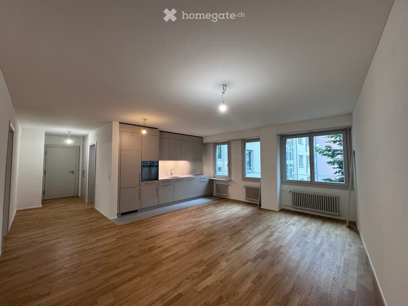 Empty room with wooden flooring, grey cabinets, and three windows. No furniture or appliances are present.
