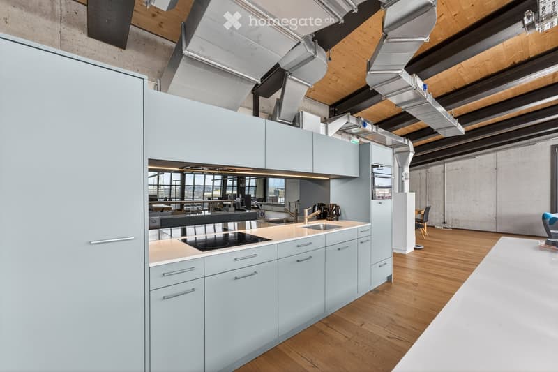 Modern kitchen with light blue cabinets, wooden flooring, stainless steel appliances, and a large window offering a view of the city.