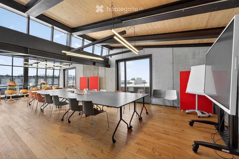 Modern office meeting room with large windows, wooden floor, long conference table, multiple chairs, and a large screen.