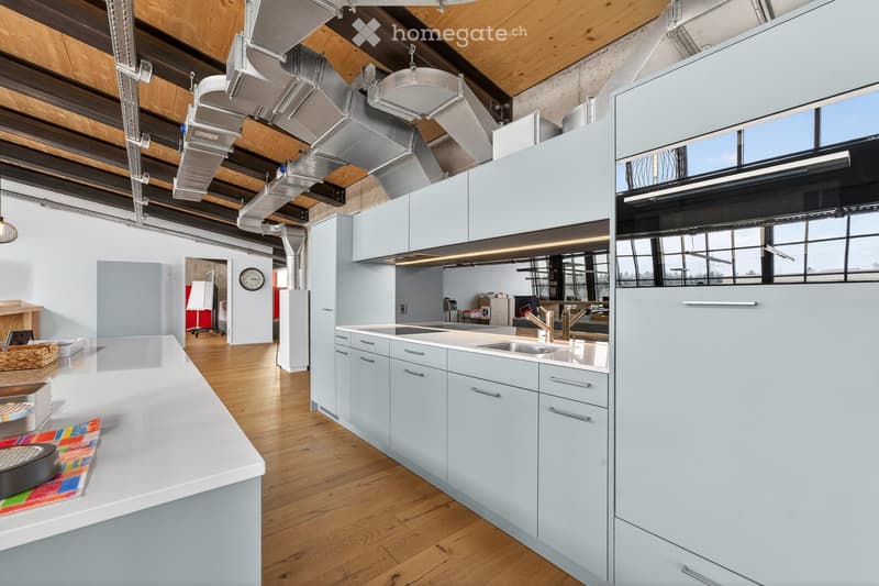 Modern kitchen with light blue cabinets, stainless steel sink, and wooden flooring. Features a large island with a white countertop, a clock on the wall, and a basket on the floor.