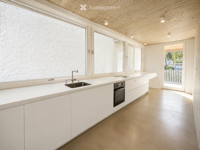 Modern, minimalist kitchen with white cabinetry, a central island, and large windows. Features a sink, faucet, and built-in oven.