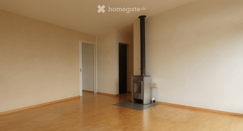 Empty room with wooden flooring, white walls, and a fireplace in the corner.