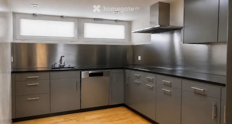 Modern kitchen with stainless steel backsplash, grey cabinets, black countertops, and a built-in dishwasher.
