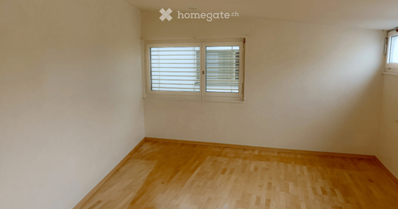 Empty room with light-colored wooden flooring and a single window with blinds.