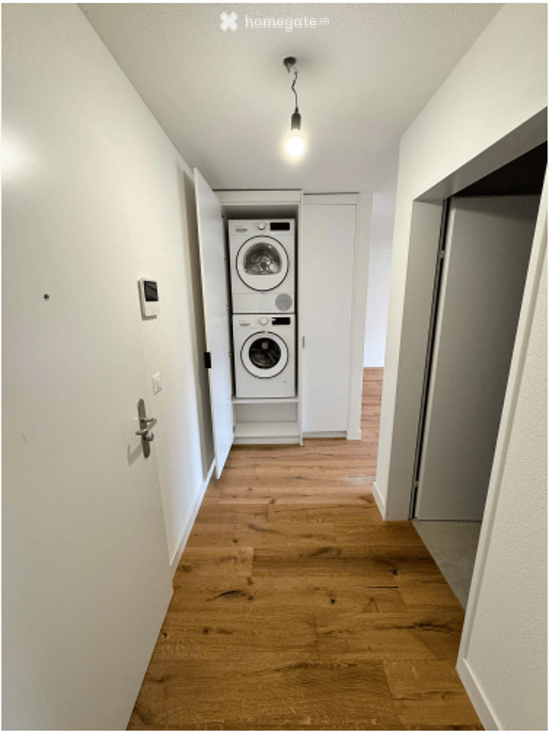 Hallway with wooden flooring, white walls, and a built-in laundry area containing a washing machine and dryer.