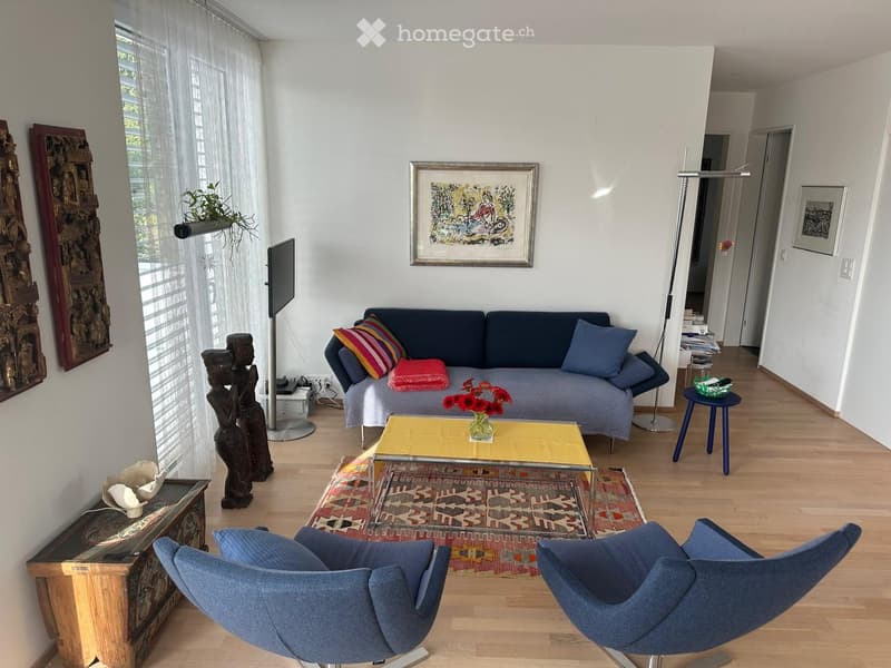 Living room with a blue sofa, coffee table, two blue chairs, a small side table, a vase with red flowers, a floor lamp, and decorative sculptures.