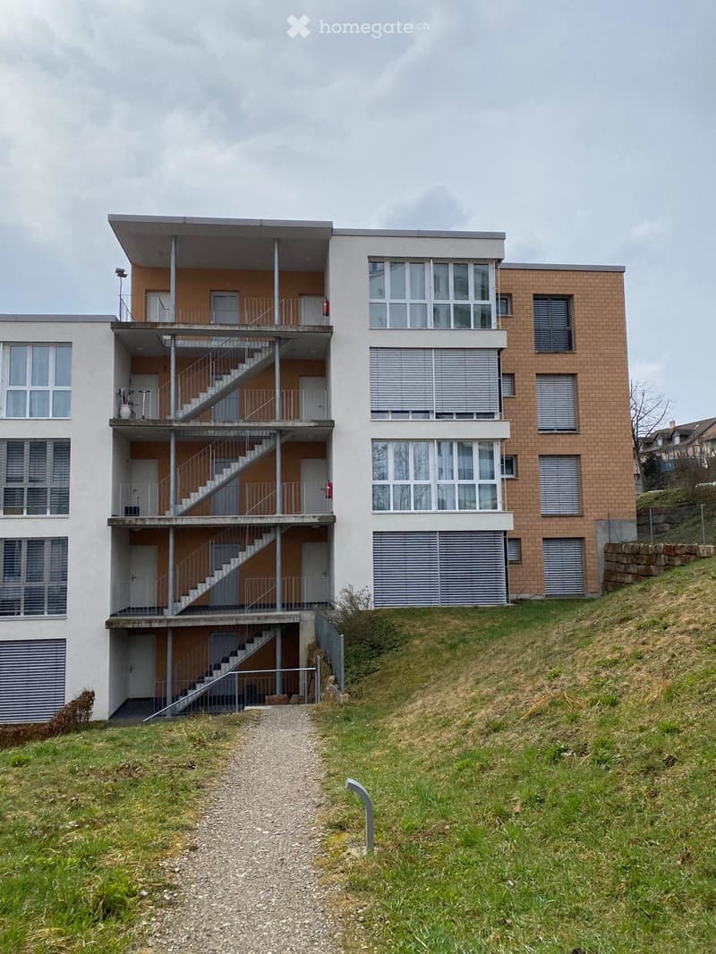 Modern two-story building with white and orange facade, large windows, and external staircase leading to upper level.