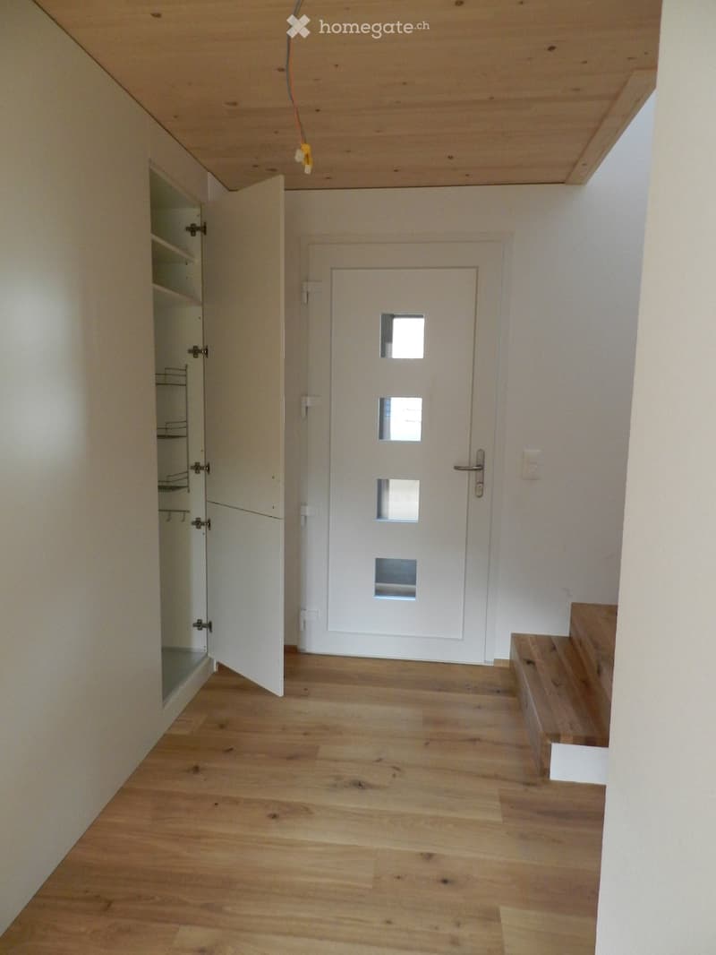 Empty hallway with wooden flooring, white walls, and a white door with glass panels at the end. A small open closet is visible on the left side.