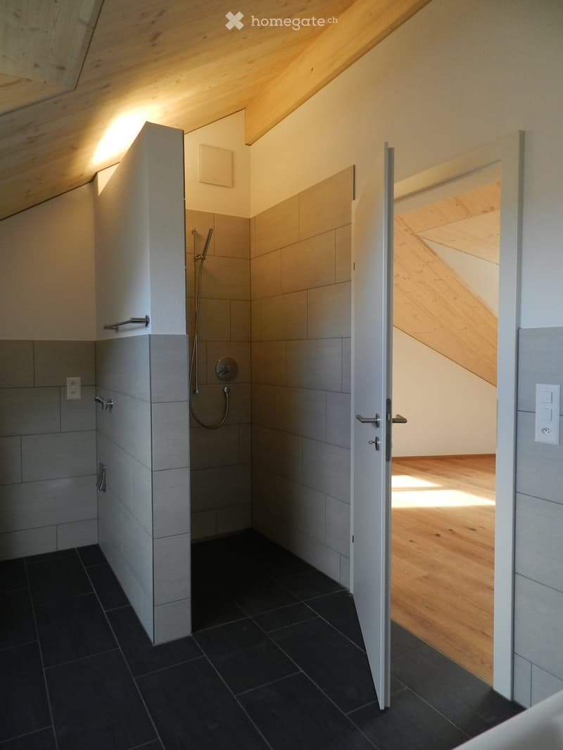 Modern bathroom with dark tiled floor, grey tiled walls, built-in shower, and white cabinetry.