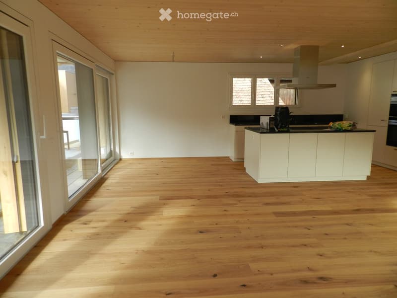 Bright, modern kitchen with light wooden flooring, white cabinets, and a central island. Large windows and sliding glass doors provide natural light and access to the outdoor area.