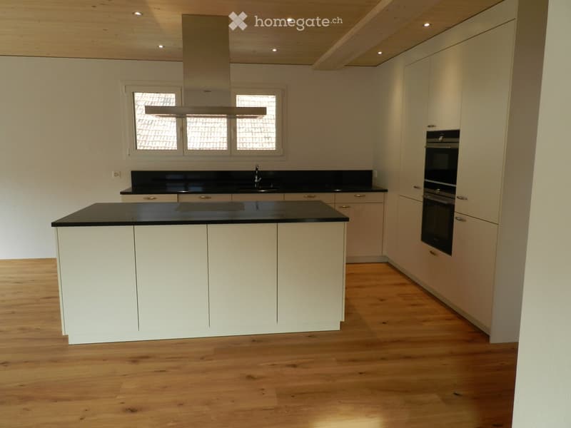 Modern kitchen with white cabinets, black countertops, and a central island. Features include a sink, built-in oven, and recessed lighting.