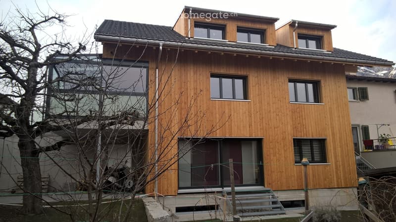Modern two-story house with wooden facade, large windows, and a raised ground floor entrance.